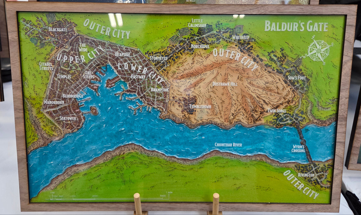 A framed relief map of Middle-earth's Baldur's Gate and Outer City, featuring raised terrain in green, brown, and blue, displayed on a stand in a shop setting.