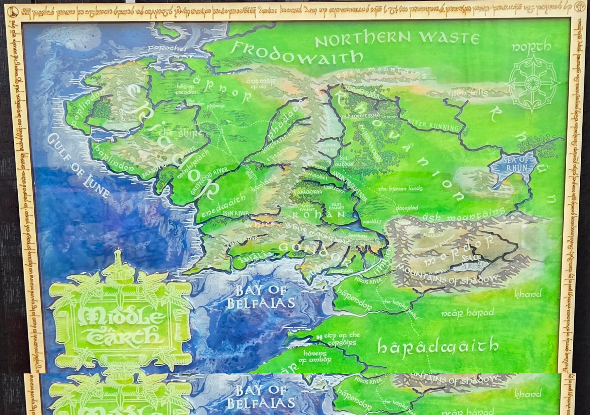 A framed fantasy map of Middle-earth, featuring green regions like Frodohwaith and Sauron, blue oceans, and labeled places from The Lord of the Rings trilogy.