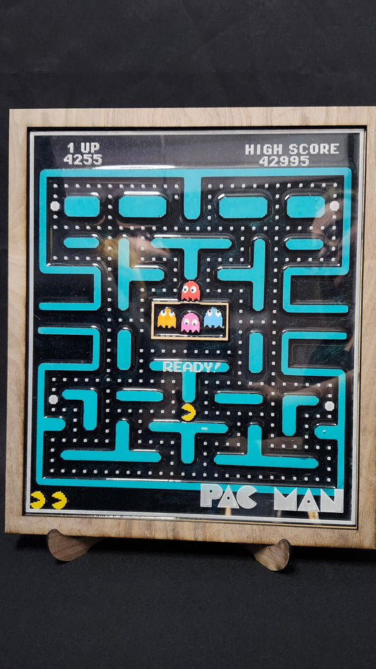 A framed retro Pac-Man arcade board game featuring the classic maze with blue paths, a yellow ghost, and red and pink ghosts, set against a dark background.